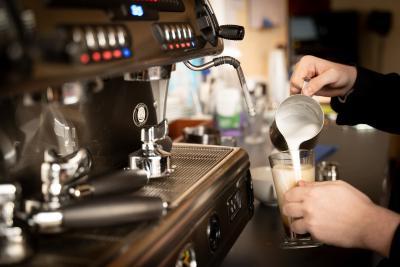 An image of hands pouring milk into a coffee